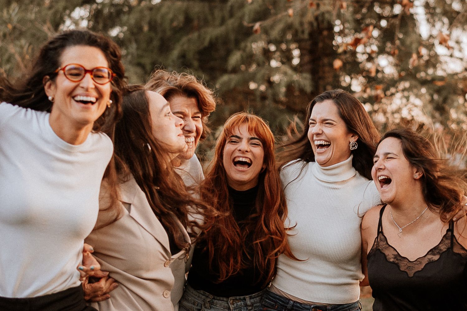 Group wearing white sweaters laughing together outdoors in natural lighting.