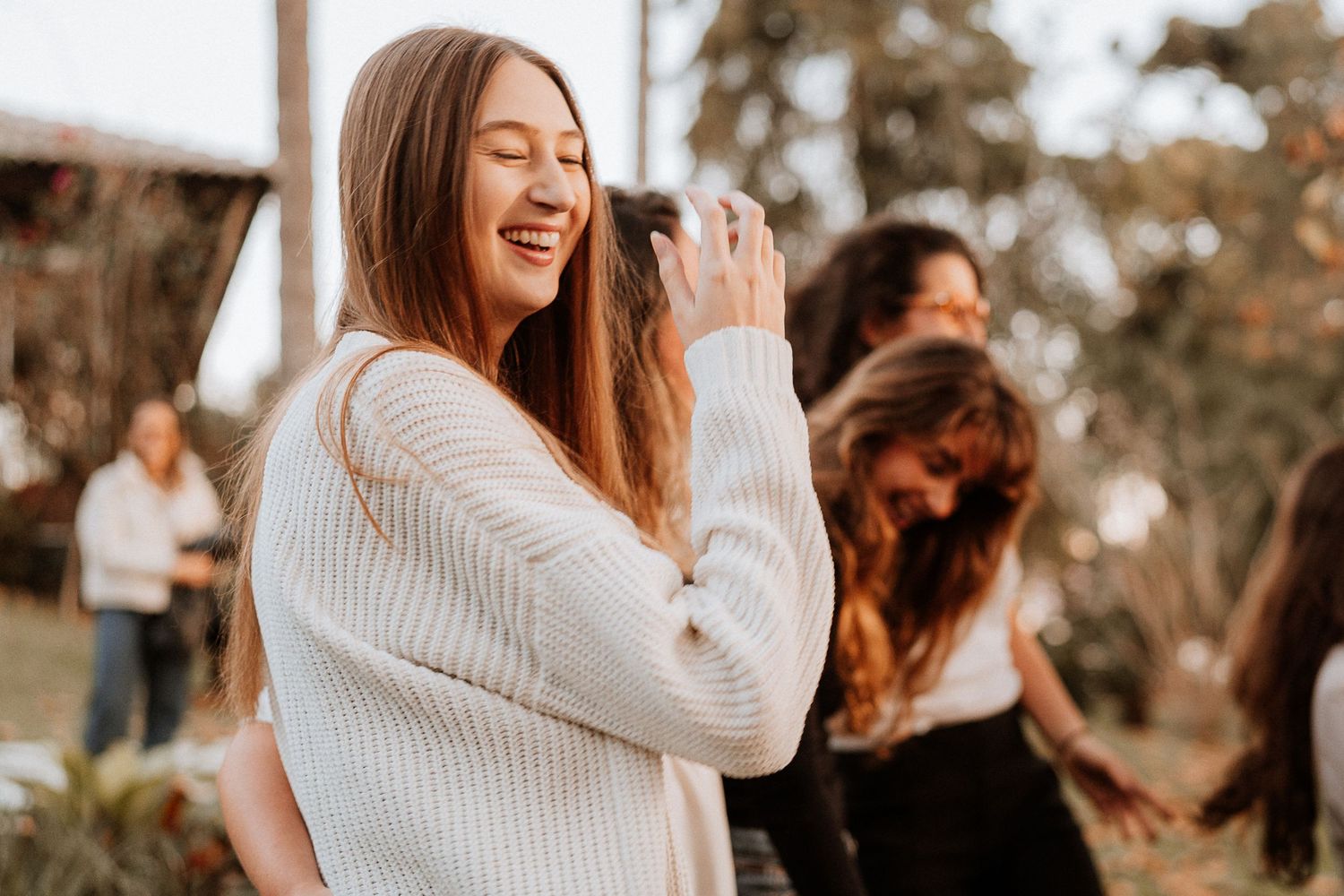 Person in white sweater laughing outdoors during photoshoot.
