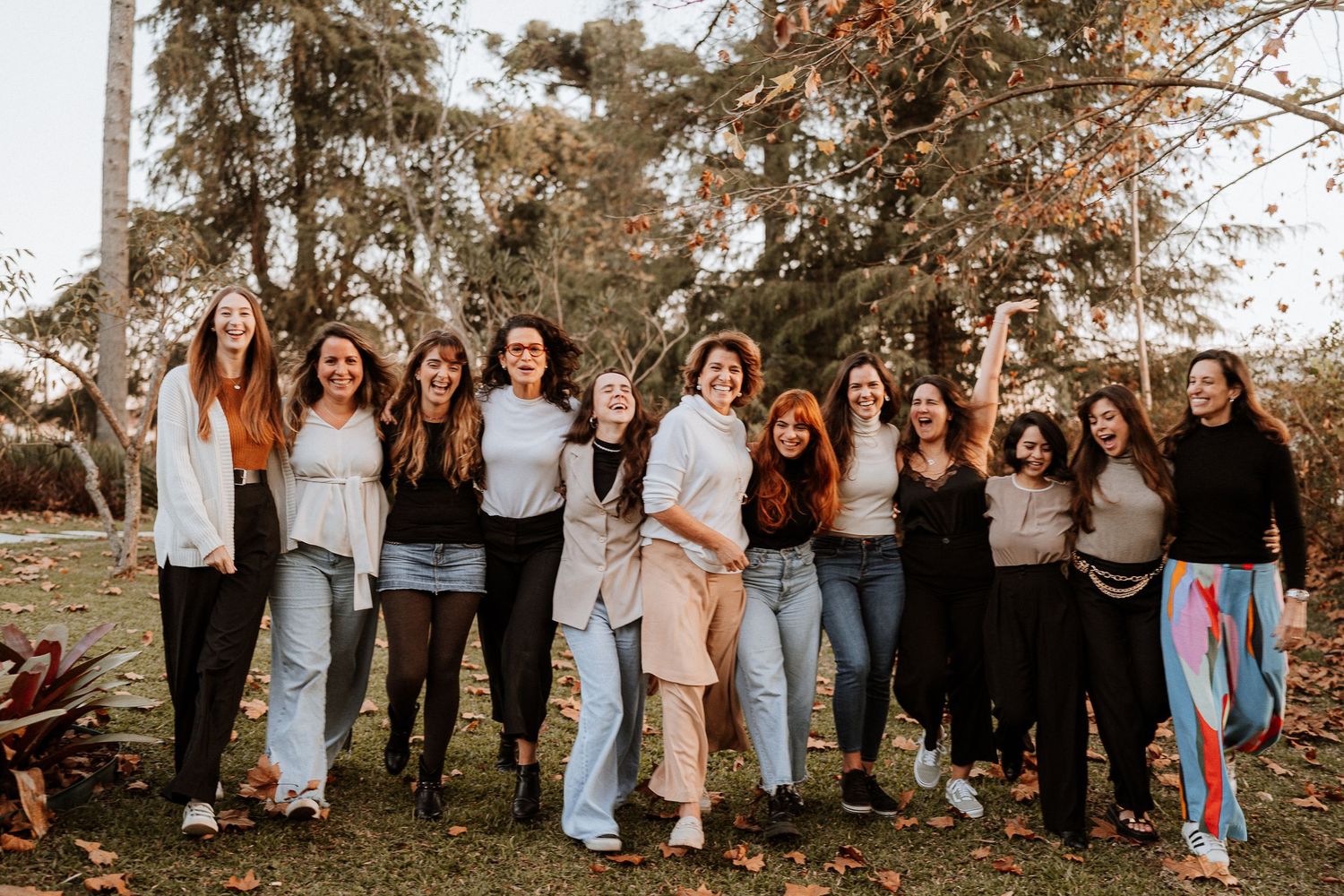 A group of friends in casual outfits laughing and posing together outdoors on an autumn day.