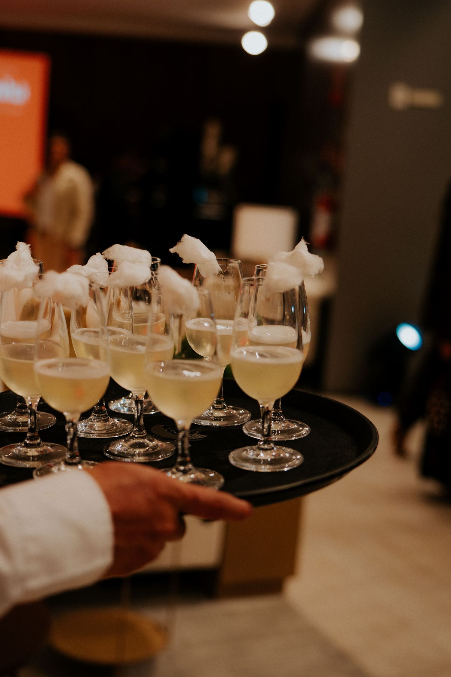 Tray of elegant cocktail glasses topped with white foam being served at an event.