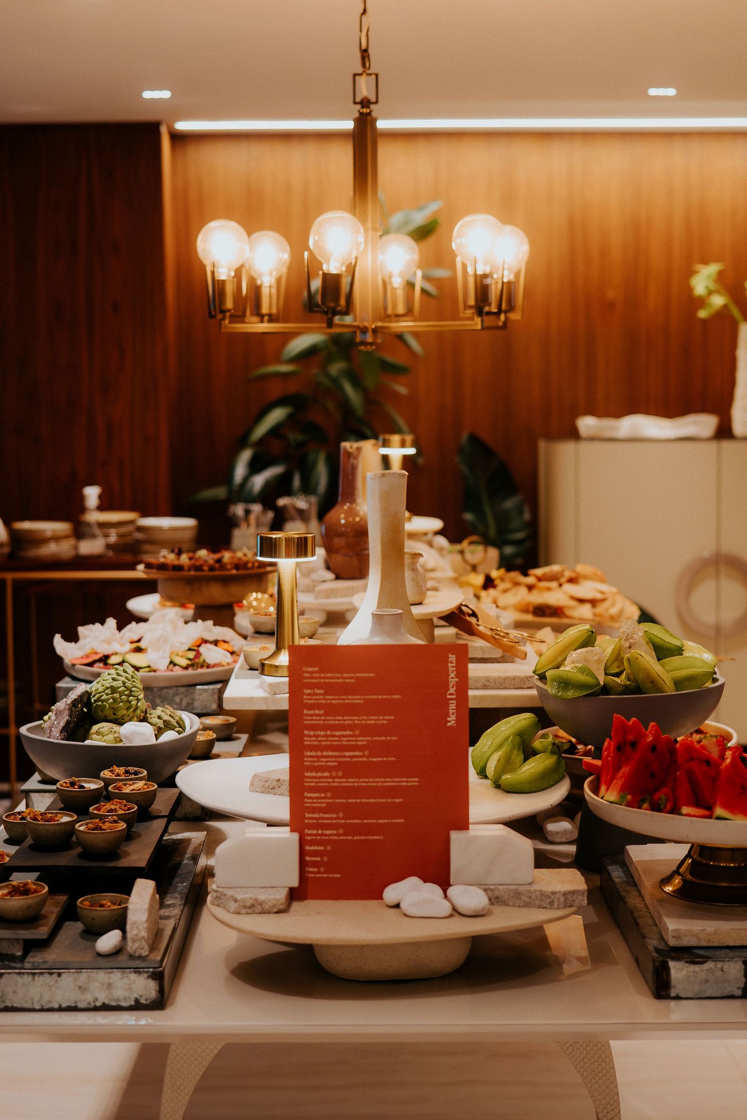 Elegant buffet spread with red menu card and modern chandelier overhead.