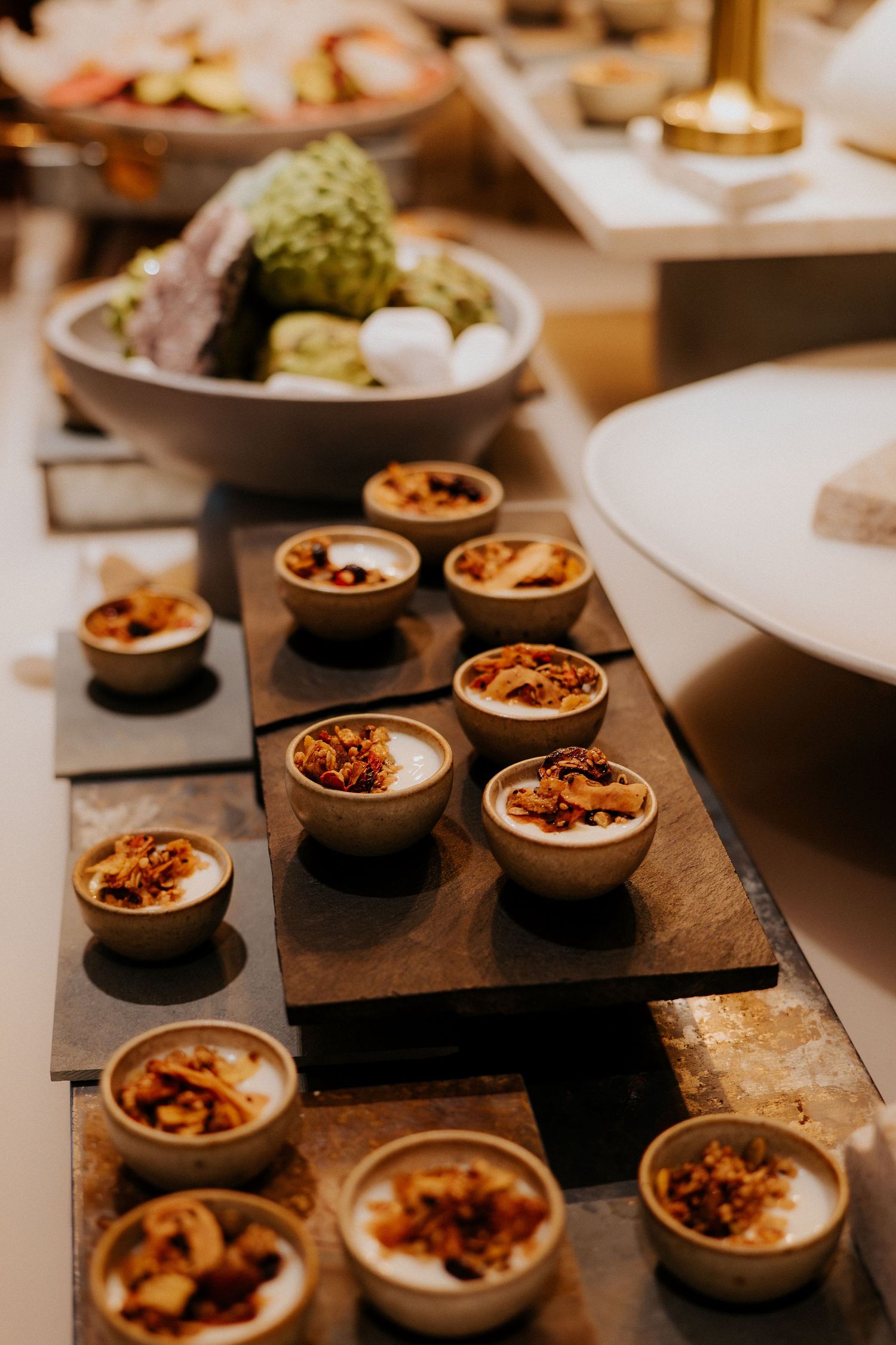 Row of small dessert cups on dark wooden serving board with garnishes.