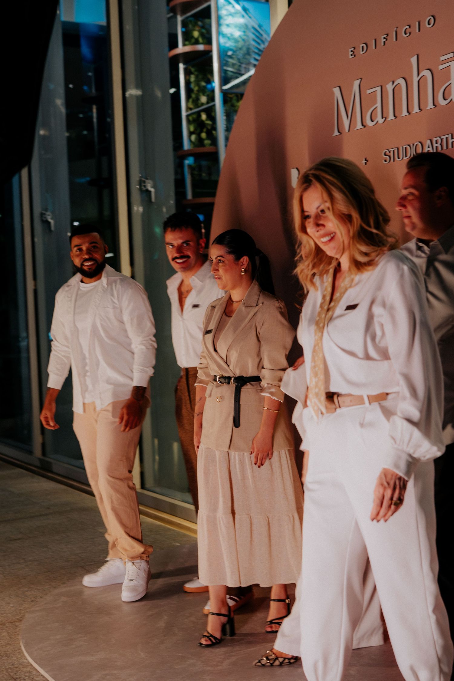 A group of people in light-colored clothing standing against a terracotta wall.