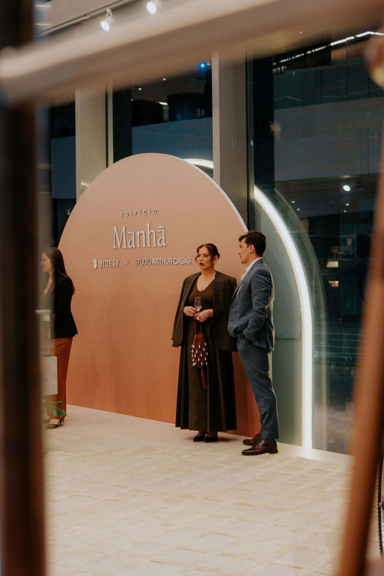 Two people standing in front of a curved pink wall with Manha signage.