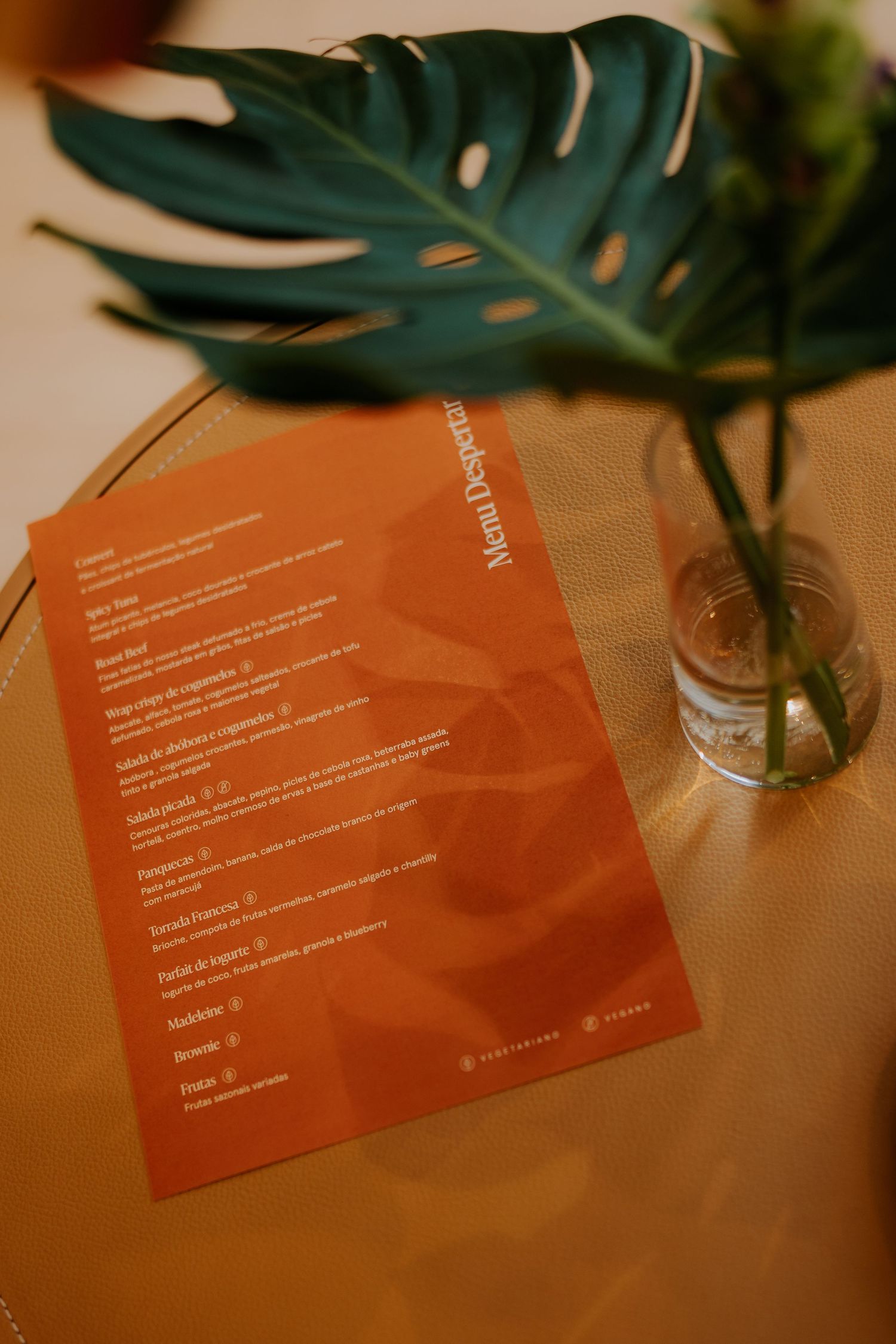 Orange menu card with monstera leaf in vase on wooden table.