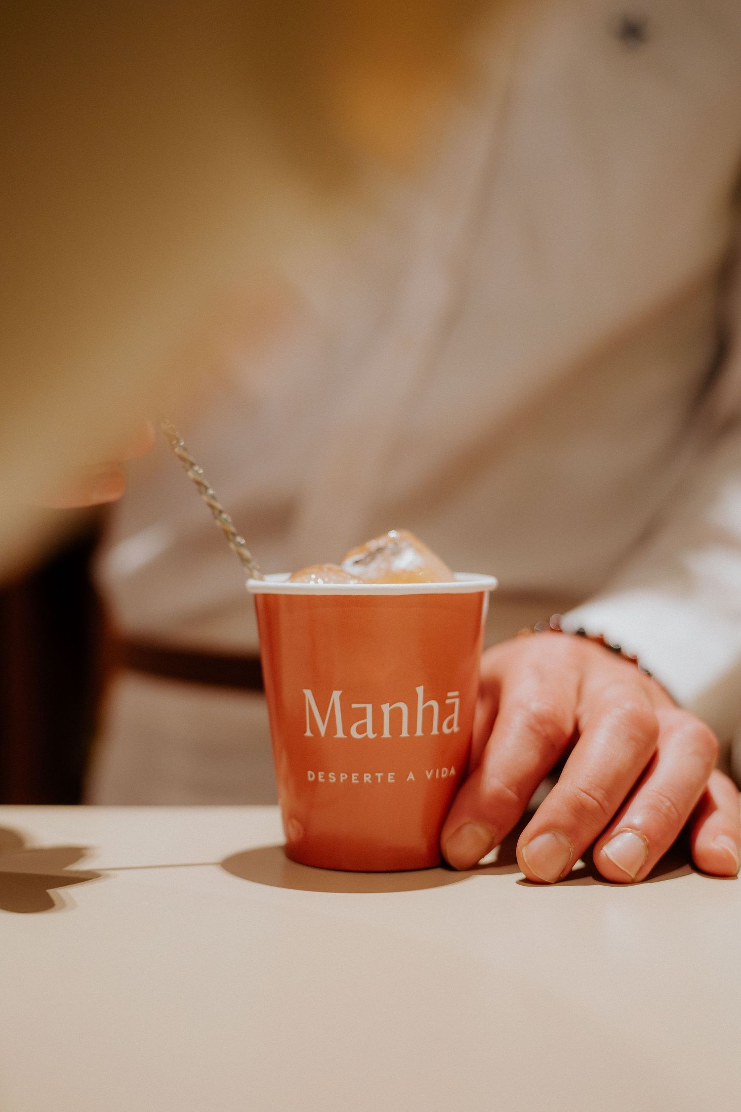 A hand reaches for a ceramic coffee cup with 'Manha' text visible.