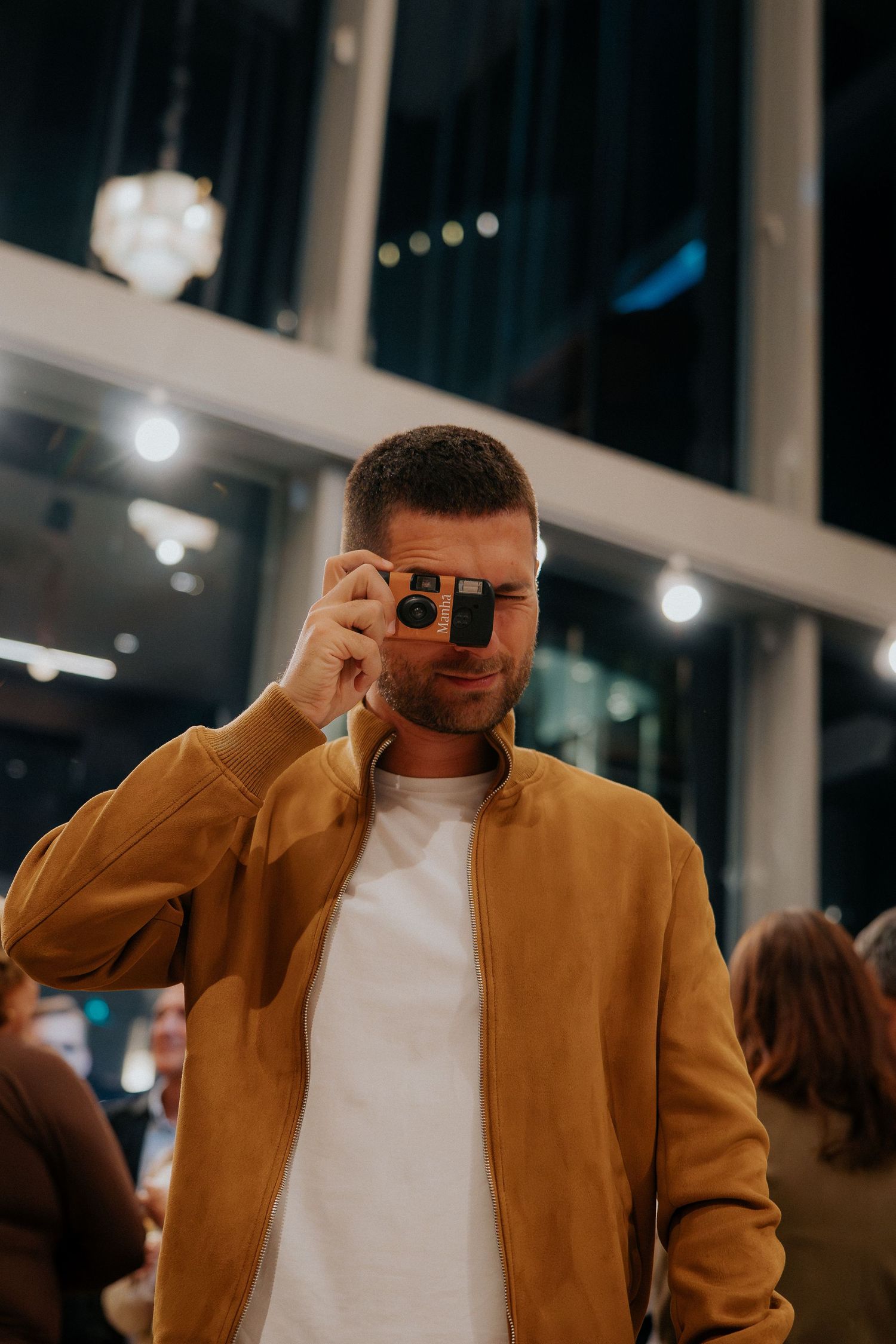 Person in brown jacket and white shirt taking pictures with a vintage camera.