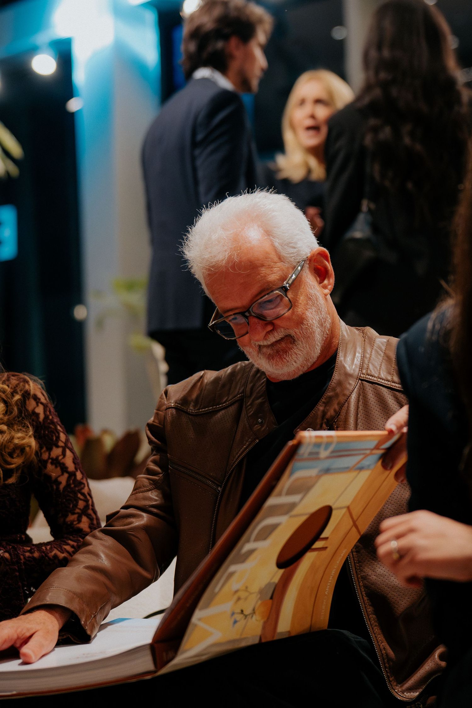 Senior person in glasses examining a book or photo album at an event.