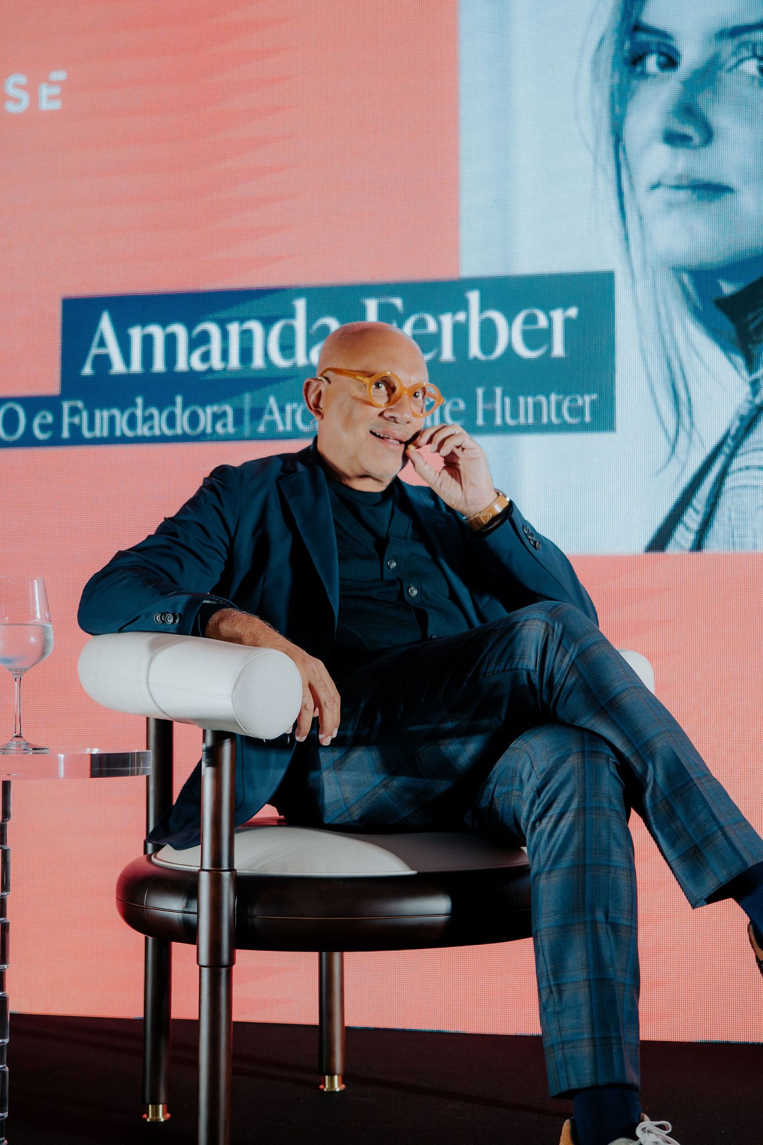 Business executive in dark suit sitting casually in white modern chair during presentation.
