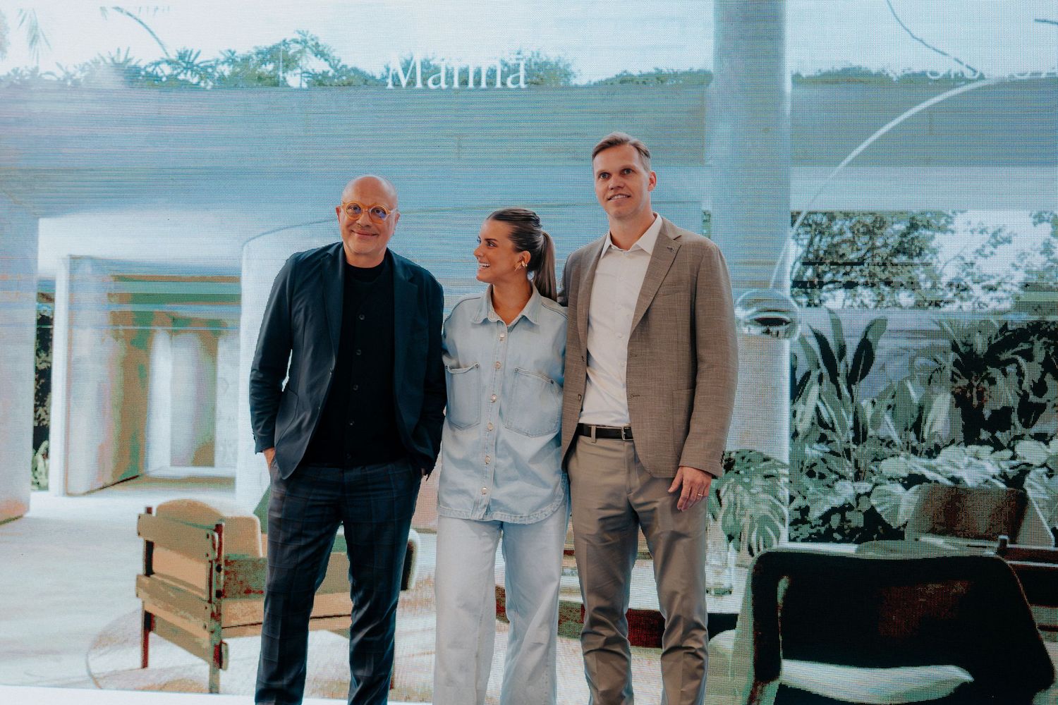 Three people standing together in casual business attire against scenic outdoor backdrop.