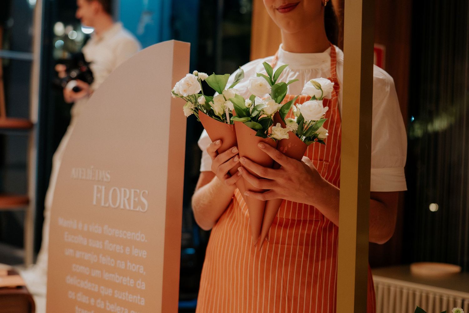 Person in coral apron holding white flower bouquet against promotional display.