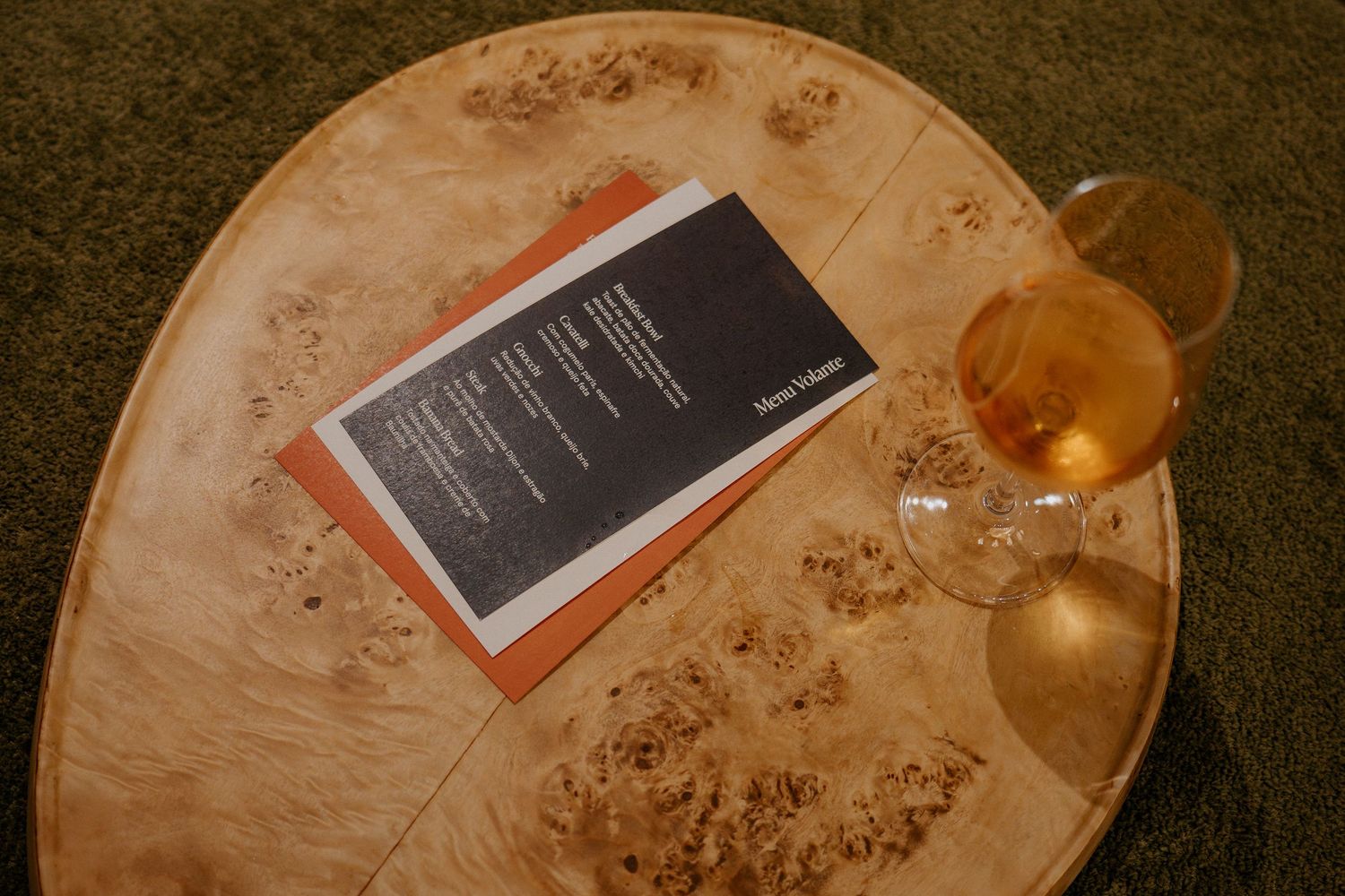 Menu card and wine glass on textured wooden table surface.
