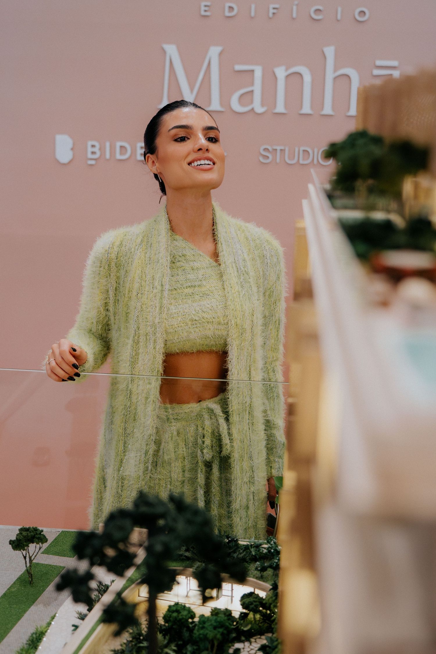 Person wearing mint green fuzzy outfit posing against pink Manha branded wall.