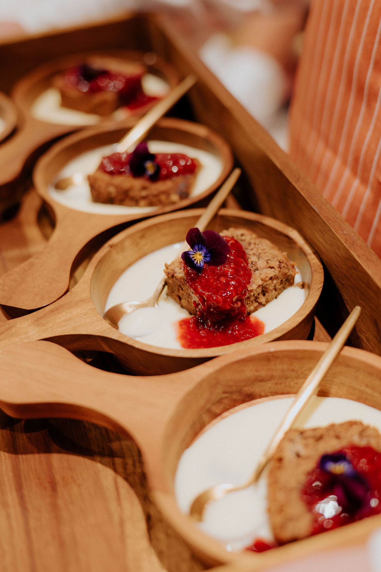 Close-up of elegantly plated desserts with red berry compote in wooden serving dishes.