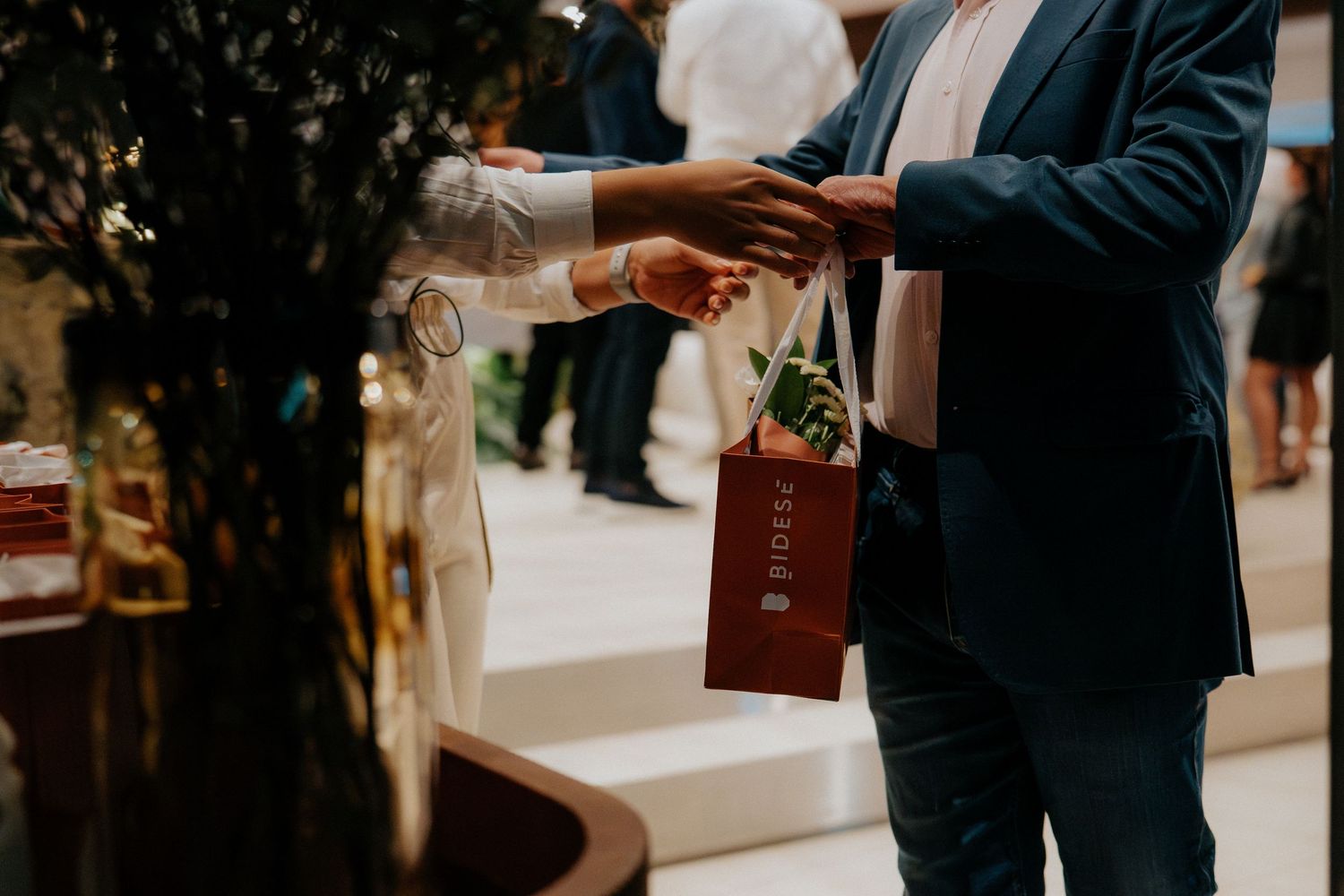 Formal event setting with guests in dark attire exchanging documents.
