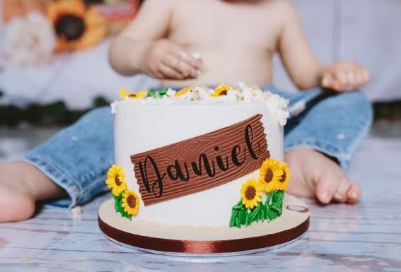 White birthday cake with decorative elements displayed on wooden slice platter.