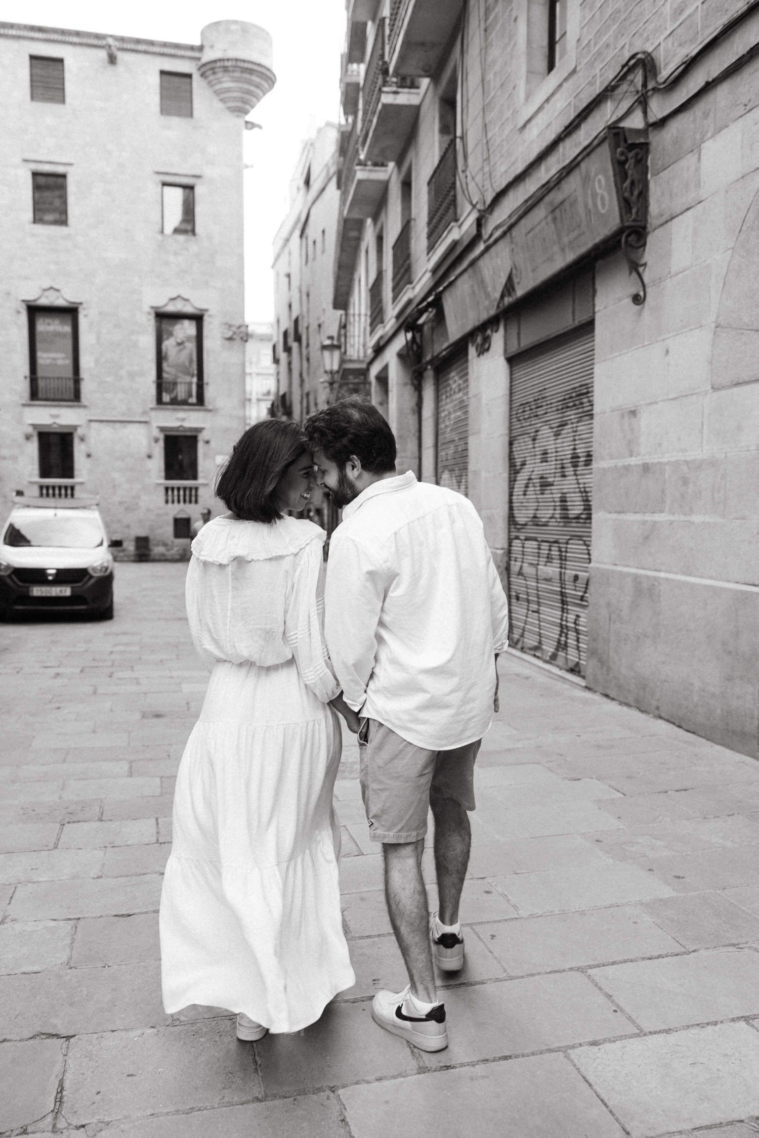 A couple walks hand in hand through narrow stone streets of an old city quarter.