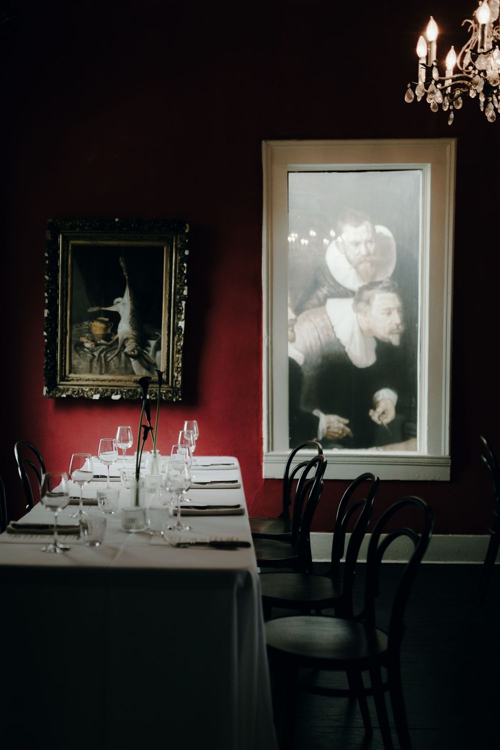 Elegant dining room setup with chandelier and framed artwork on deep red walls.