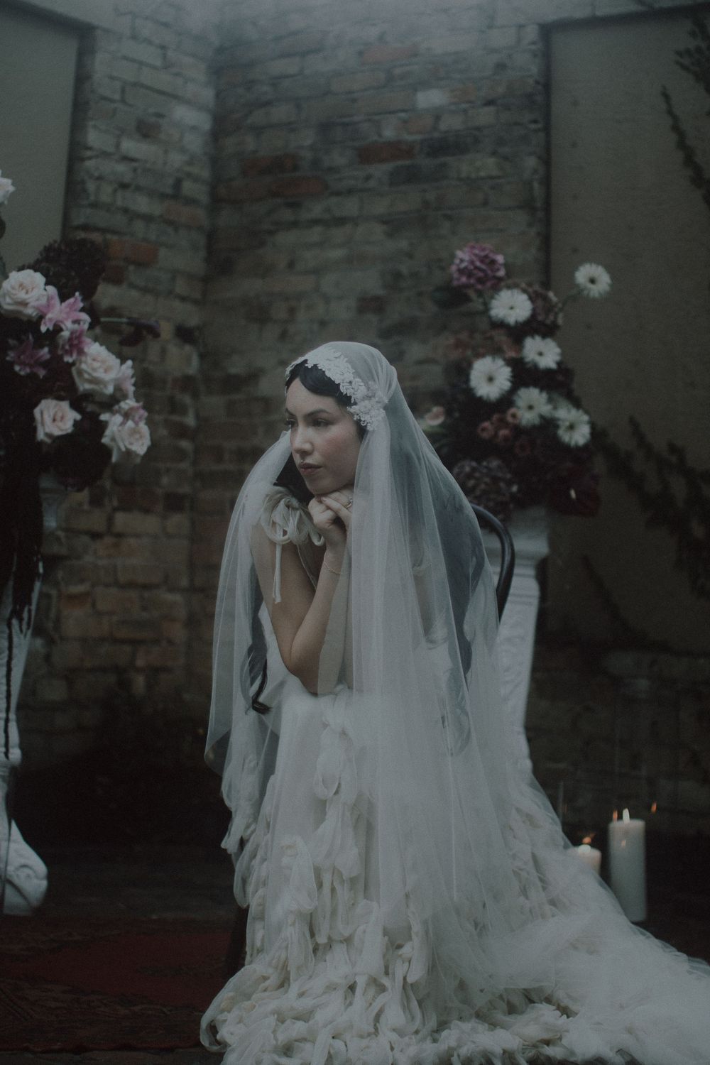 A romantic bridal portrait with delicate lace veil and floral backdrop in moody lighting.