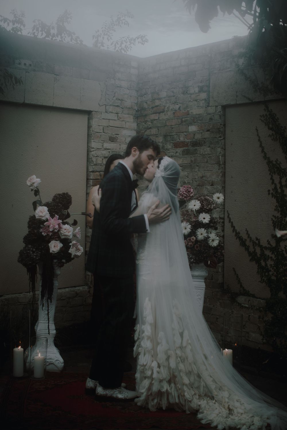 A romantic wedding scene against a brick wall backdrop with elegant floral arrangements and a flowing white gown.