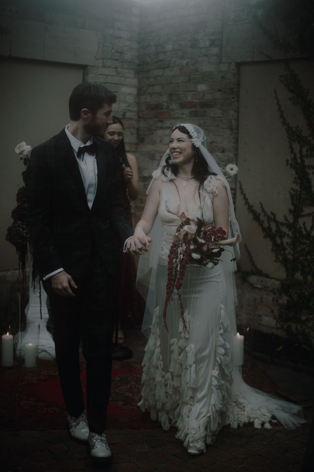 An intimate wedding moment unfolds against a rustic brick wall setting with delicate floral decor.