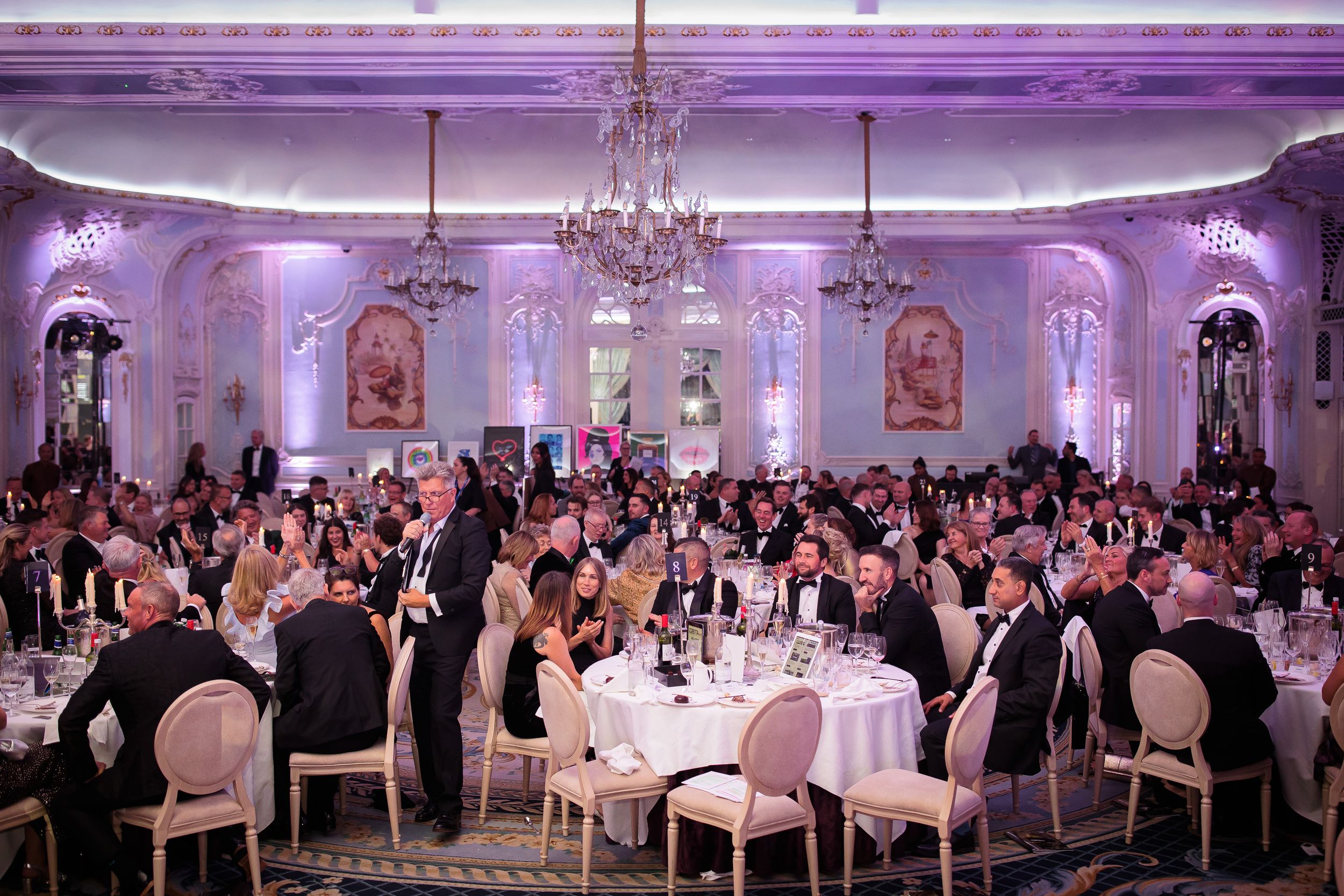 Elegant ballroom decorated in purple uplighting with formal table settings for a gala event.