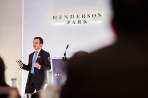 Business presentation at Henderson Park with speaker gesturing to audience in professional setting.