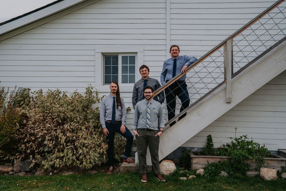 Wedding party members strike dynamic poses on stairs of white barn building.