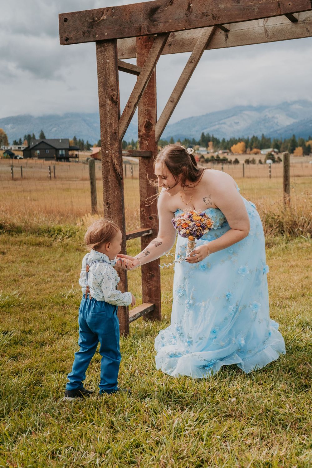 A light blue formal dress flows in the breeze as people interact in a rustic outdoor setting with wooden beams.