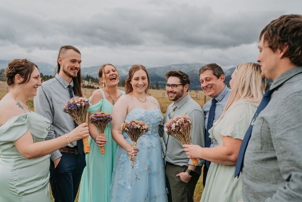 Wedding party in mint green and gray attire laughing together outdoors under cloudy skies.