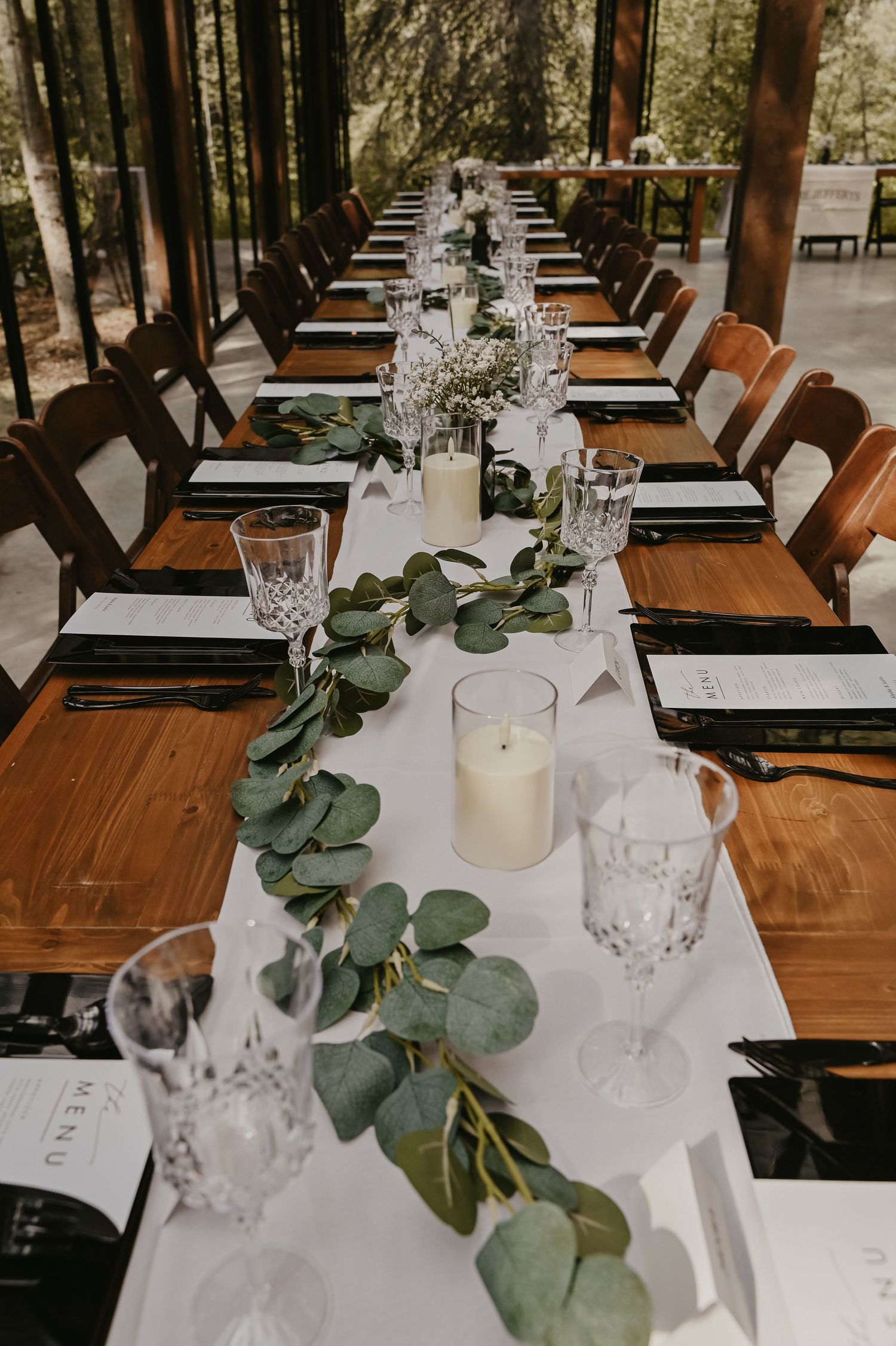 Elegant wedding reception table settings with eucalyptus garlands and crystal glassware.
