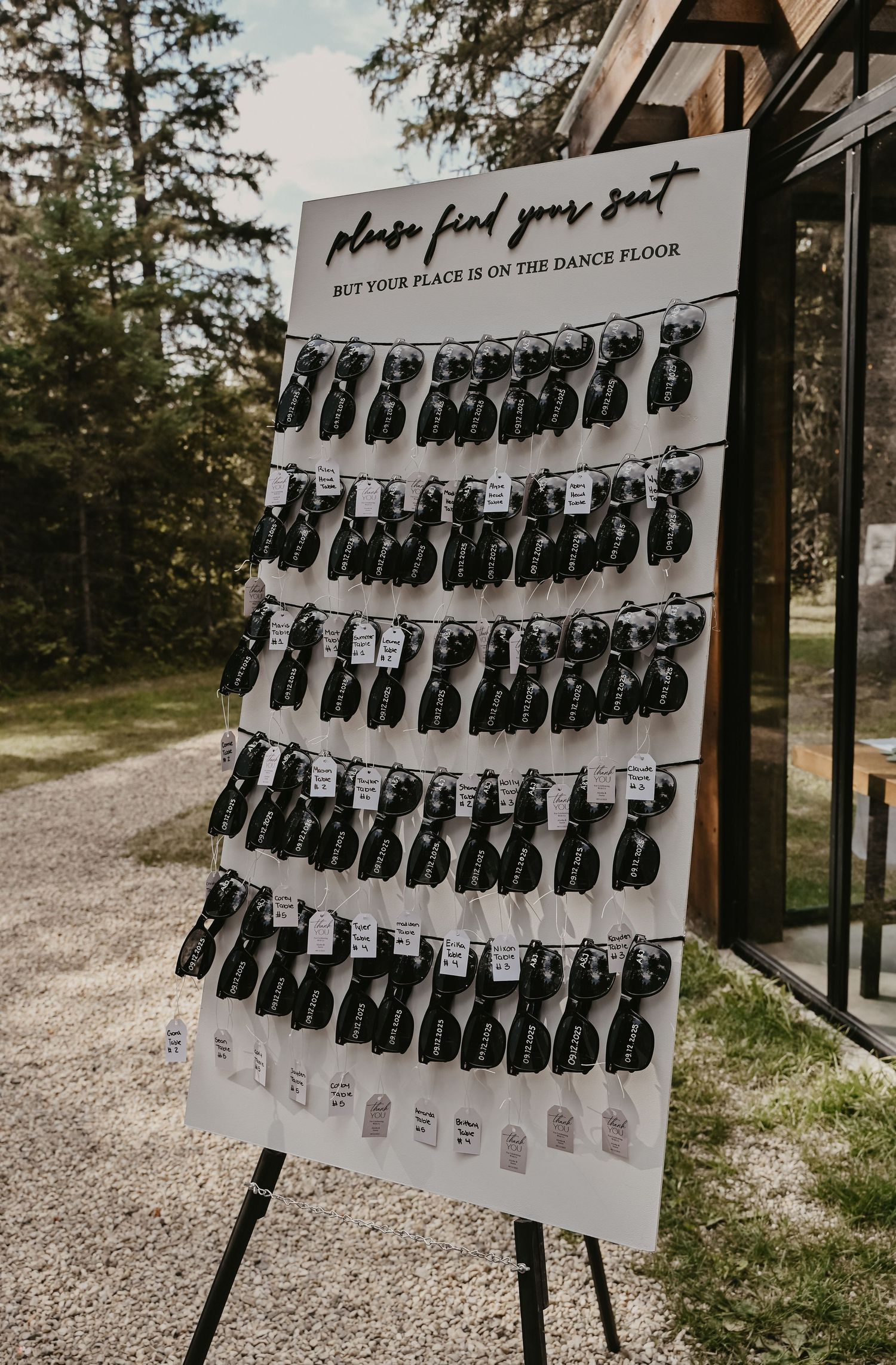 Wedding seating chart display with black and white name cards arranged in rows on an elegant easel stand at outdoor venue.