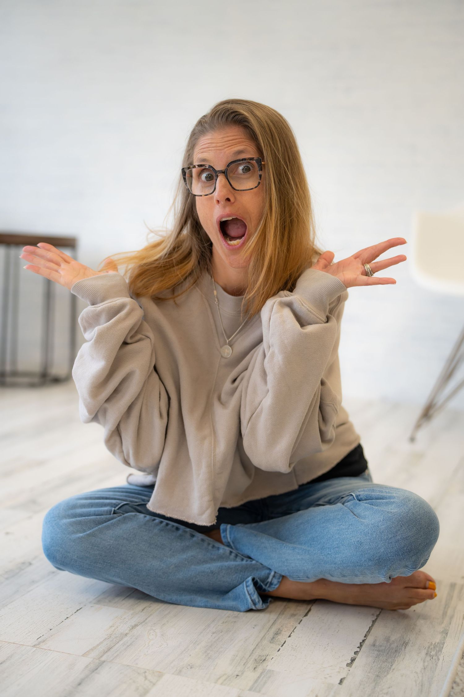 Expressive portrait showing animated gesture while sitting cross-legged in casual attire.