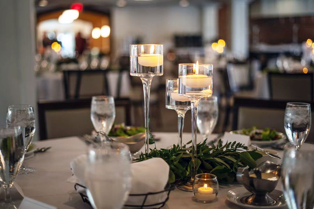 Elegant wedding reception table setting with floating candles in stemmed holders and greenery garland centerpiece.