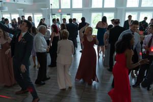 Wedding reception guests mingle and dance in a modern venue with floor-to-ceiling windows.