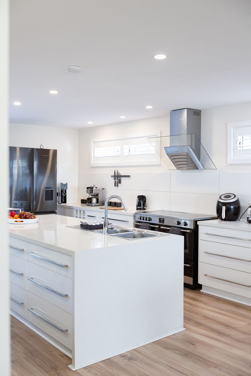 Modern white kitchen with sleek handleless cabinets, stainless steel appliances and light wood flooring.