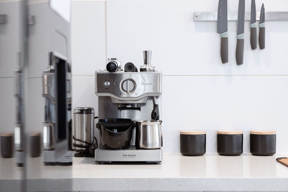 Modern kitchen appliances including coffee makers and grinders arranged in a sleek minimalist white space.
