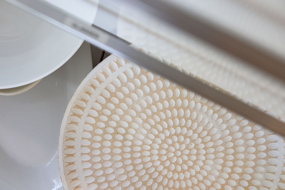 A series of images showing the process of creating a spiral pattern on a white clay or ceramic surface.