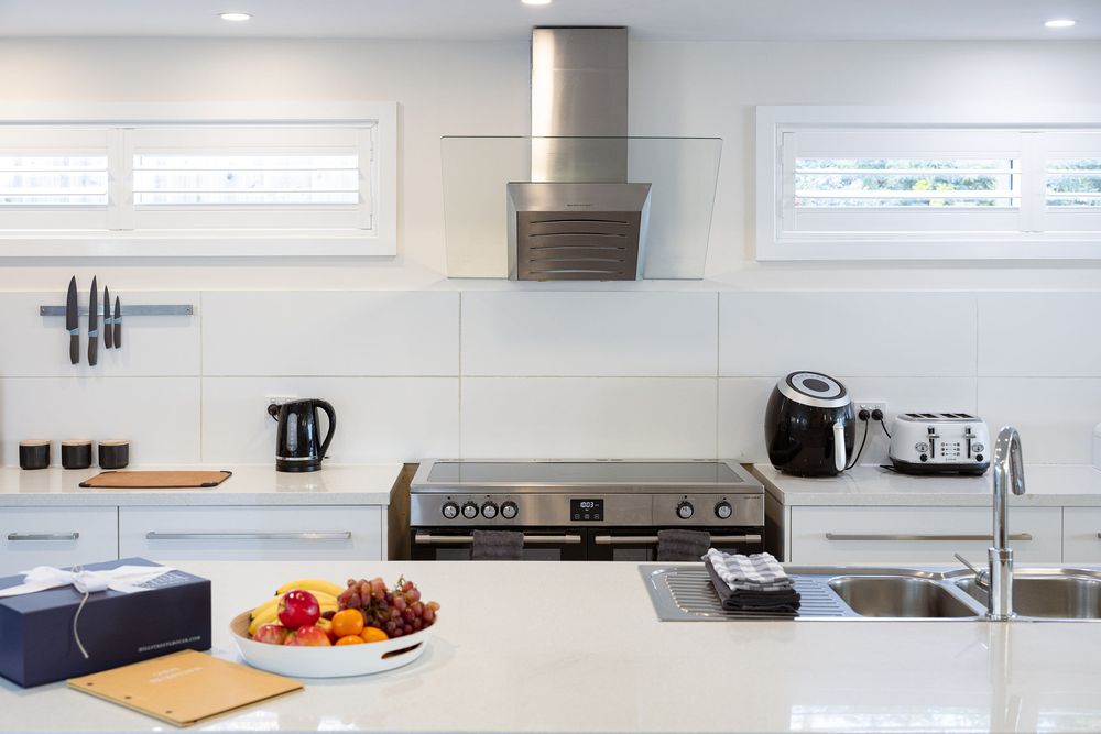 Modern white kitchen with recessed lighting, stainless steel appliances and clean minimalist design features.