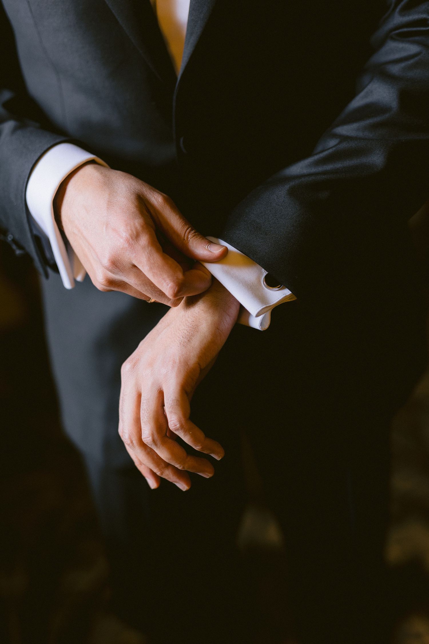 Close-up sequence of hands in a dark suit adjusting cuff links against black background.
