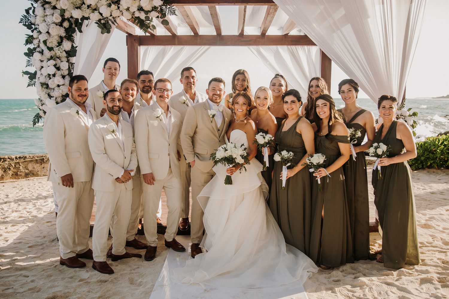 Wedding party members in neutral beige and brown attire pose together on a sunny beach for formal photos. El Dorado Royale Wedding Photograp