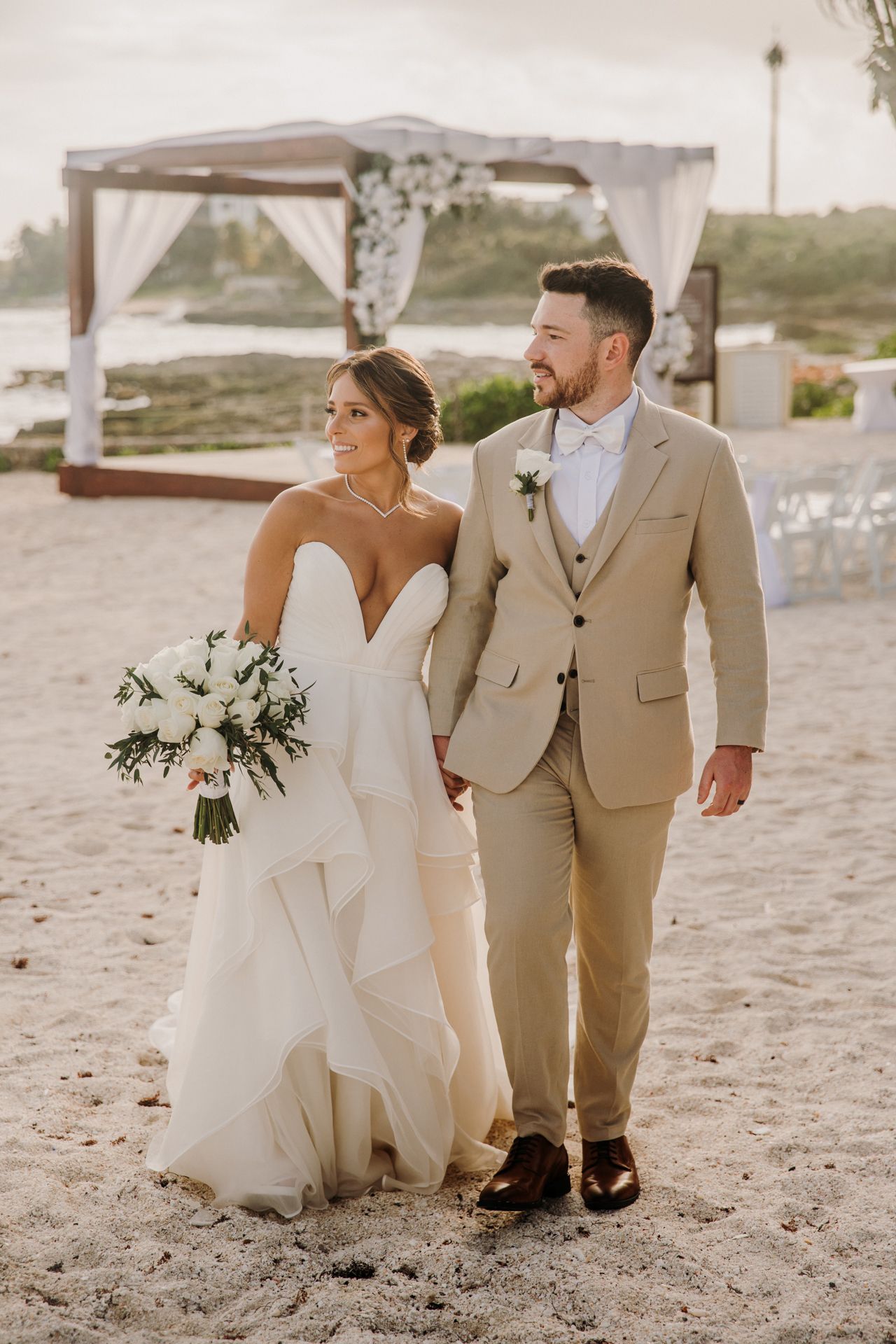 Newlyweds in white and beige attire pose playfully together on a sandy beach during their destination wedding. El Dorado Royale Wedding