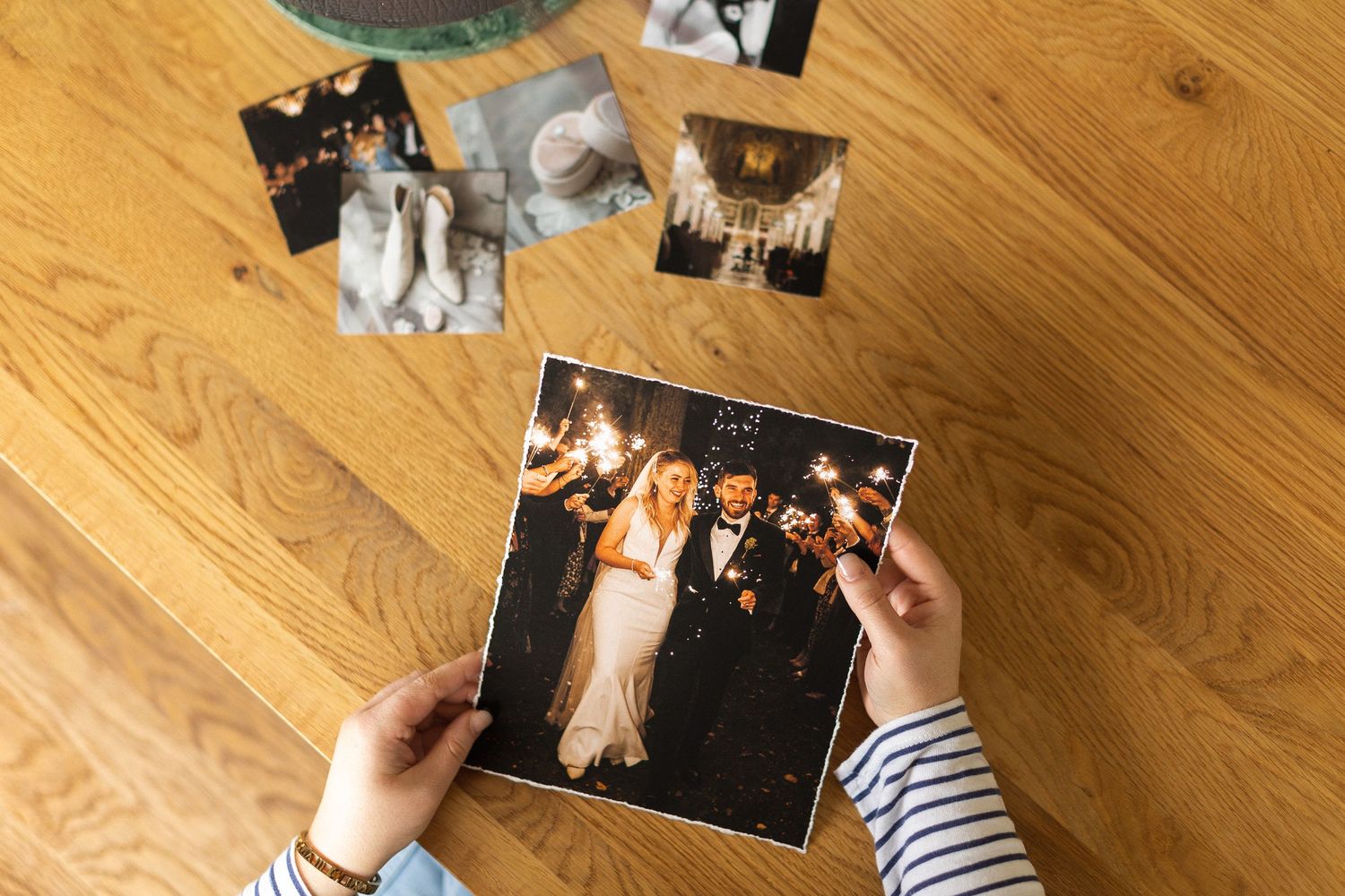 Someone's hands arranging vintage black and white photographs on a wooden floor surface.
