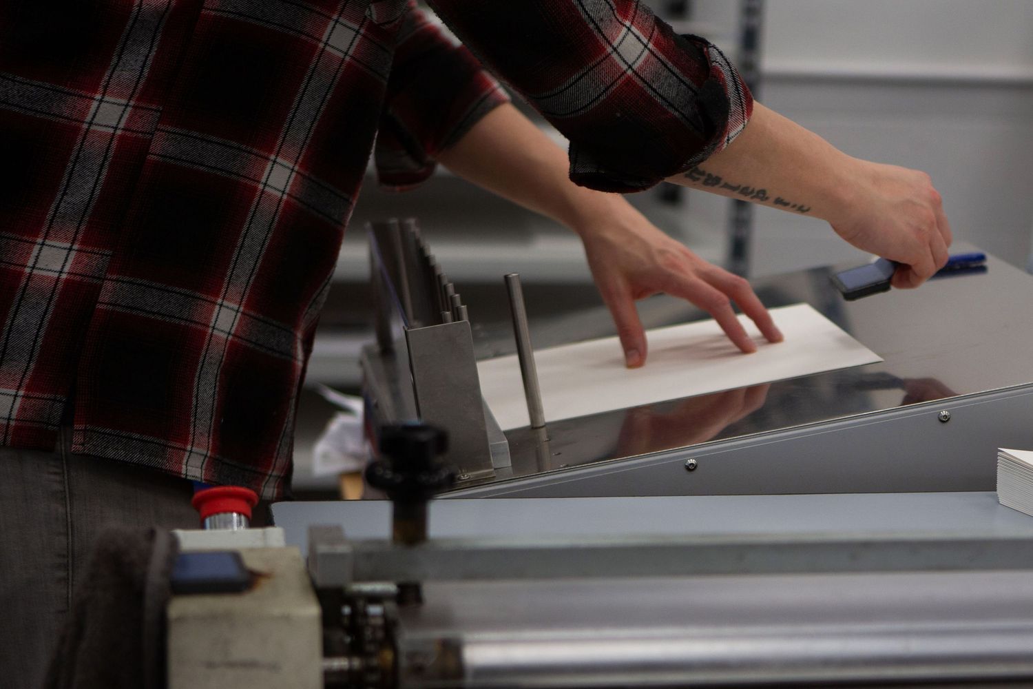 Person wearing plaid shirt operates a table saw to cut wood in a workshop setting.