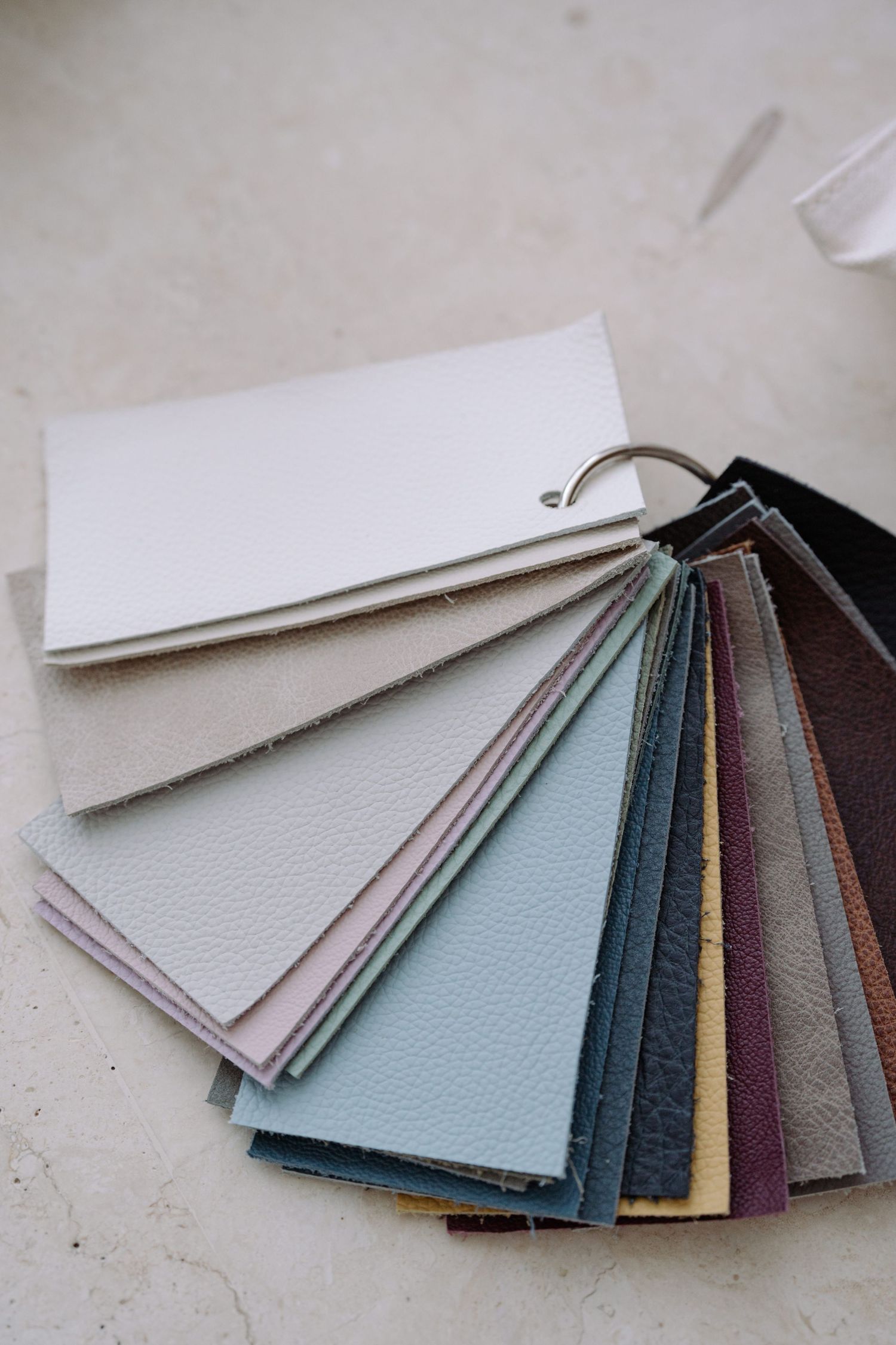 A fan of leather material swatches in various colors including white, blue, and brown connected by a metal ring.
