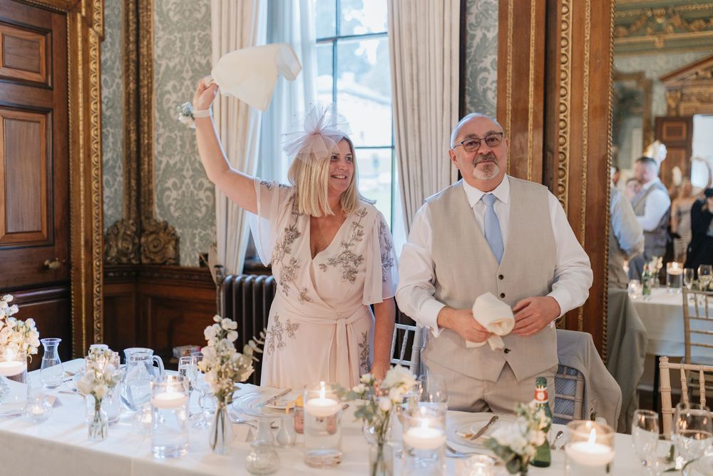 Wedding guests enjoying a formal dinner reception in an elegant ballroom with ornate decor and chandeliers.