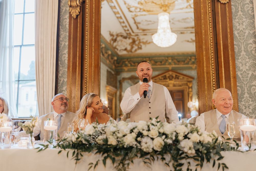 A group of people laughing and celebrating at an elegant wedding reception with ornate decor and floral arrangements.
