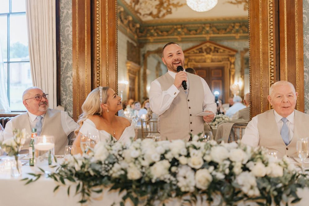 White floral arrangements and table settings adorn a luxurious ballroom during a wedding celebration.