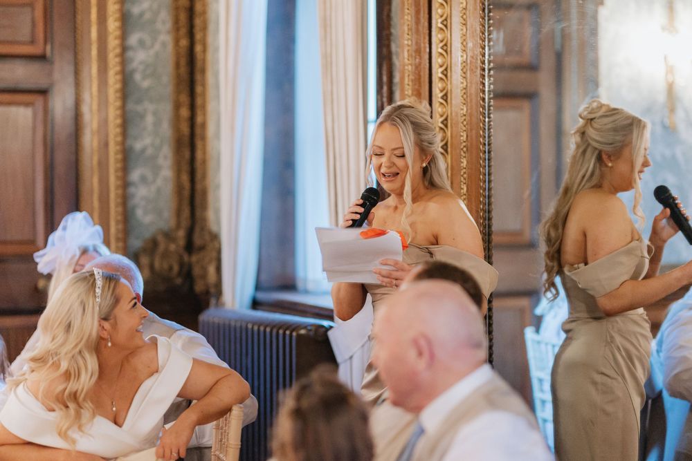 Wedding party celebrates joyfully in an elegant room with ornate mirrors and decorative moldings.