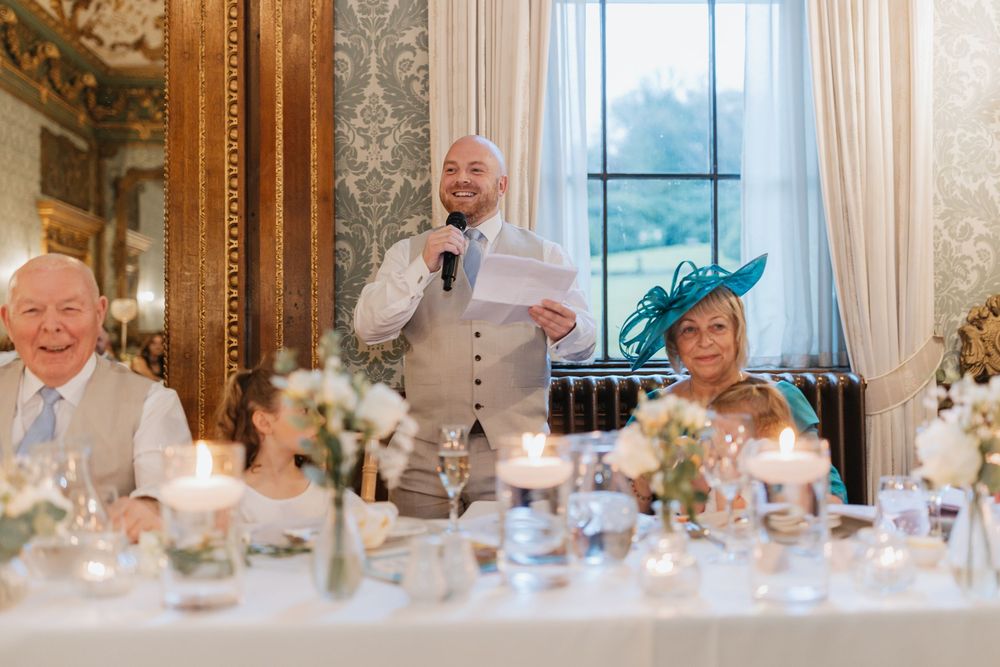 Wedding guests seated at long tables in an elegant ballroom with ornate decor and floral centerpieces.